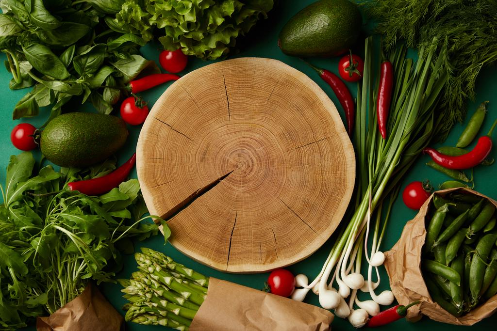 top view of wood cut surrounded with different ripe vegetables on green surface - Photo, Image