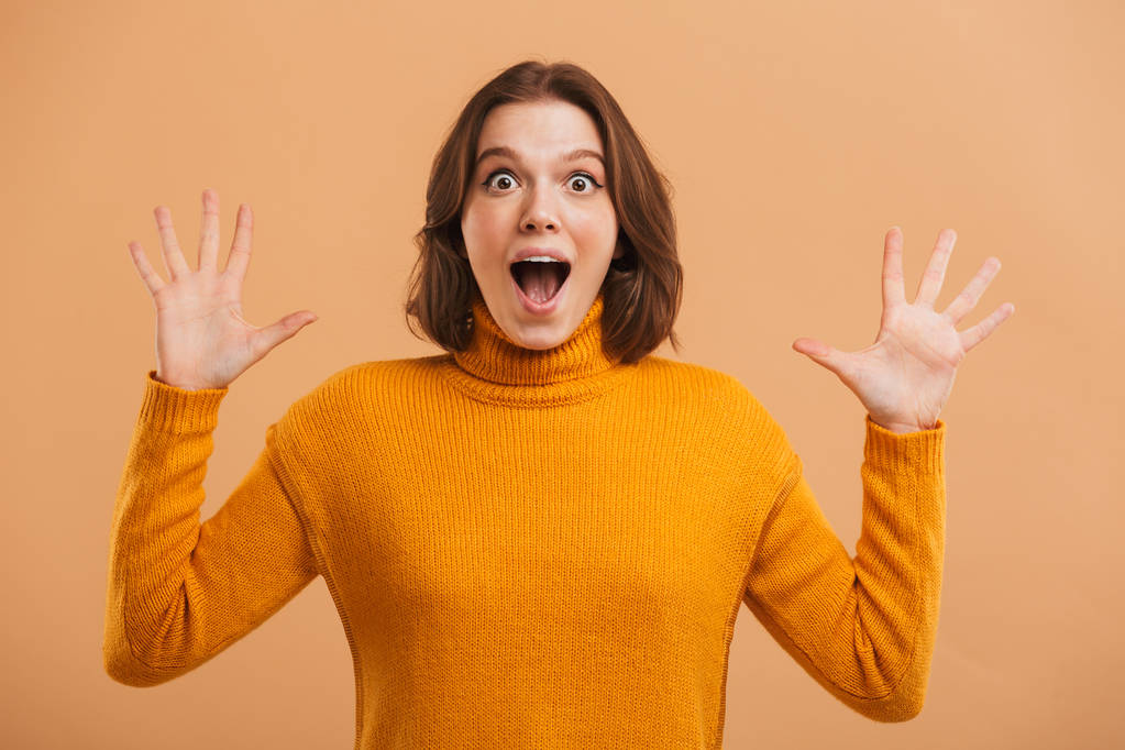 Portret van een enthousiast jonge vrouw in trui vieren van succes op beige achtergrond - Foto, afbeelding