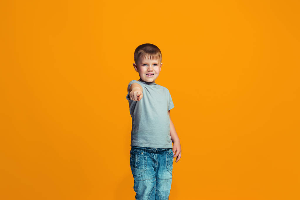Le garçon adolescent heureux pointant vers vous, portrait de gros plan à mi-longueur sur fond orange
. - Photo, image