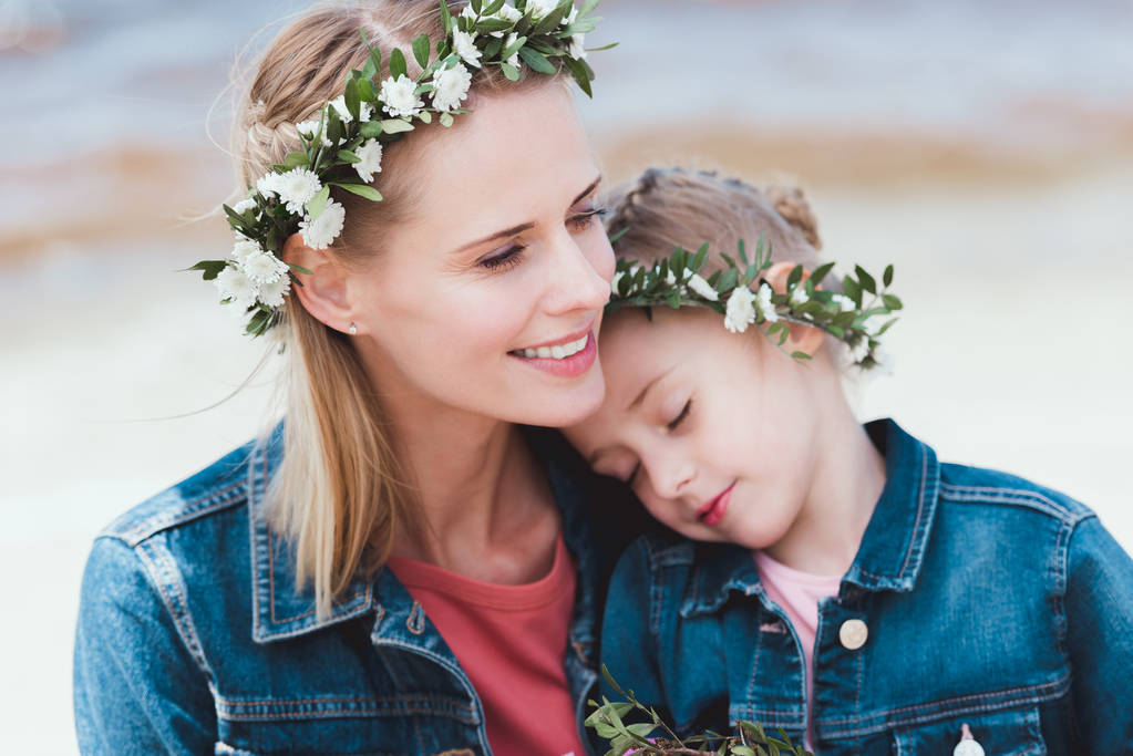 Χαμογελώντας η μητέρα και κόρη στην floral στεφάνια που αγκαλιάζει την ακτή - Φωτογραφία, εικόνα