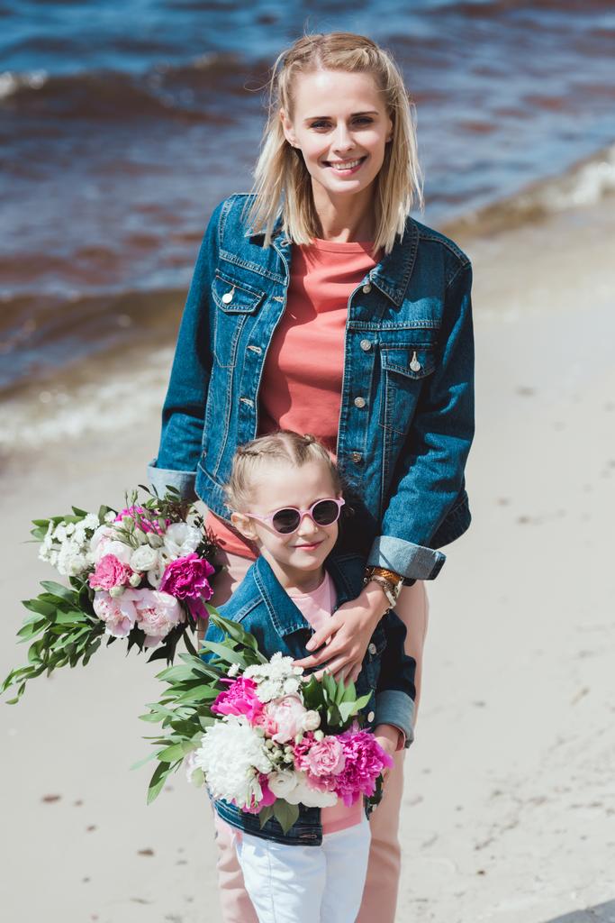 mother and daughter with peony bouquets on sea shore - Photo, Image