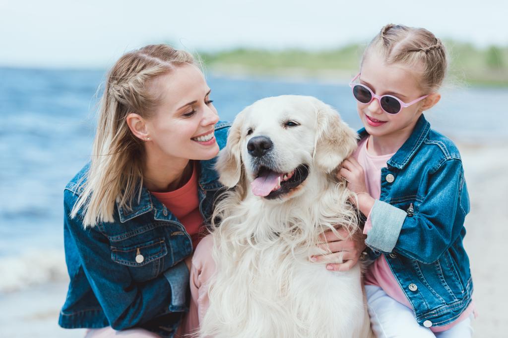 smiling mom and daughter with golden retriever dog on sea shore - Photo, Image