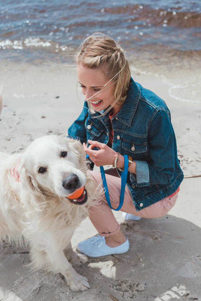 blonde woman playing with golden retriever dog on sandy shore - Photo, Image