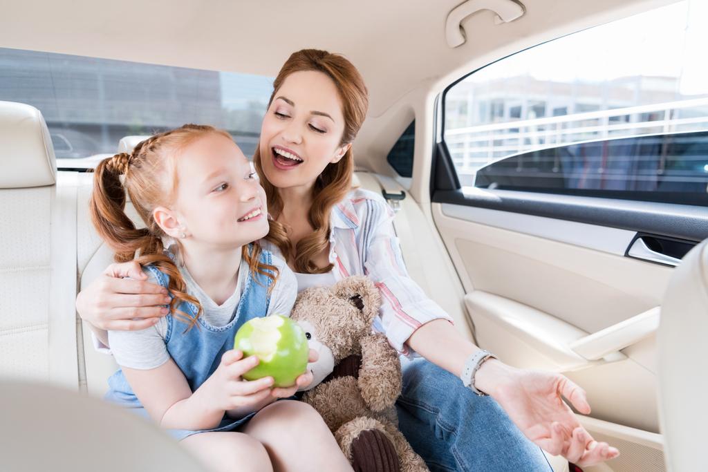 onnellinen äiti ja tytär nallekarhu ja omena istuu autossa
 - Valokuva, kuva