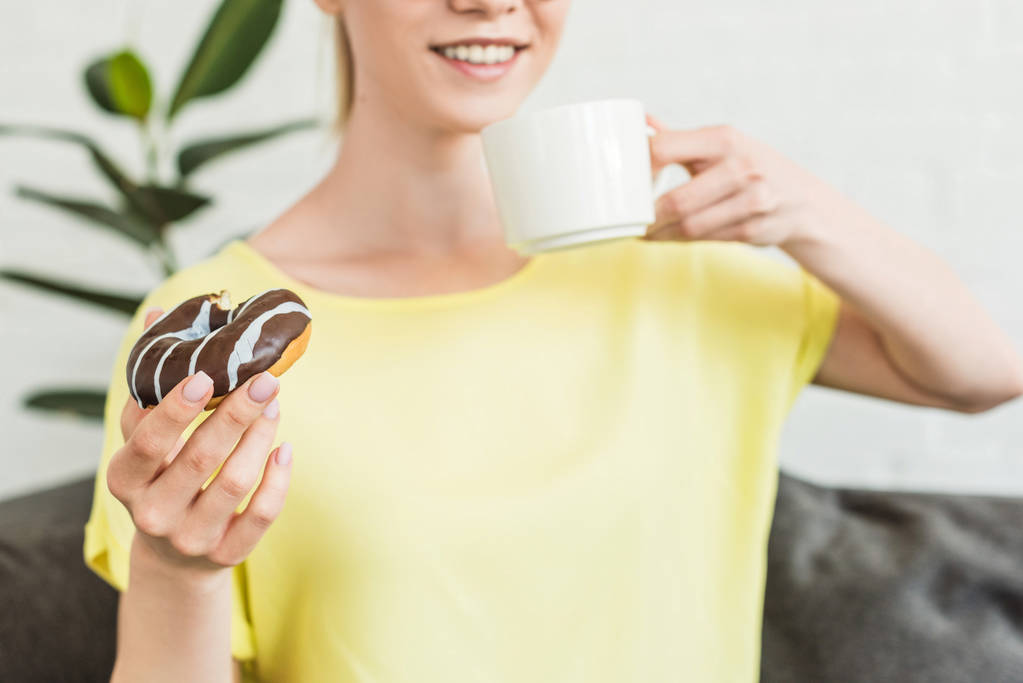 corte tiro de jovem bebendo café e comer donut em casa
 - Foto, Imagem