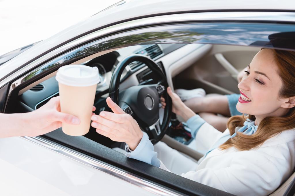 Улыбающаяся деловая женщина в машине берет кофе, чтобы уйти от продавца
 - Фото, изображение