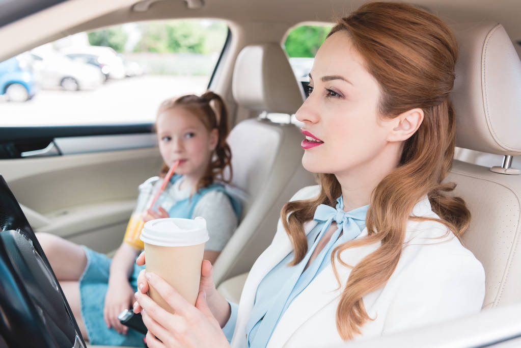 foco seletivo de mulher de negócios com café para ir e filha com suco perto no carro
 - Foto, Imagem