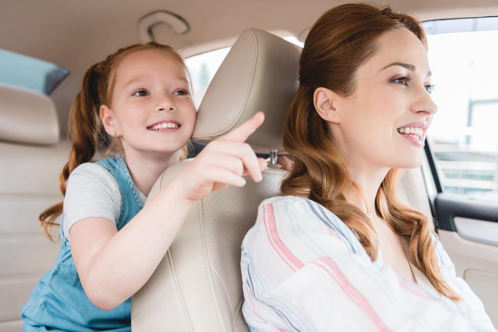side view of smiling kid pointing away and mother driving car - Photo, Image