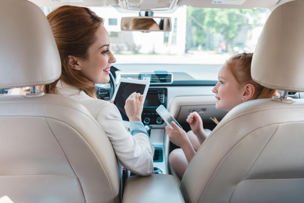 visão traseira da família sorridente com dispositivos digitais no carro
 - Foto, Imagem