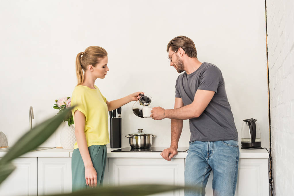vista lateral de la mujer vertiendo café a novio en la cocina
  - Foto, imagen