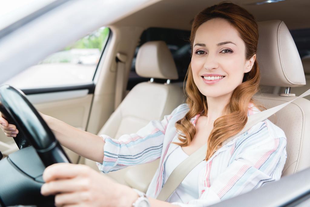 вид збоку усміхненої жінки дивиться на камеру під час водіння автомобіля
 - Фото, зображення