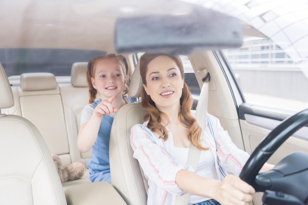 portrét usmívající se žena, která řídila auto a dceru ukazující daleko na sedadla cestujících - Fotografie, Obrázek