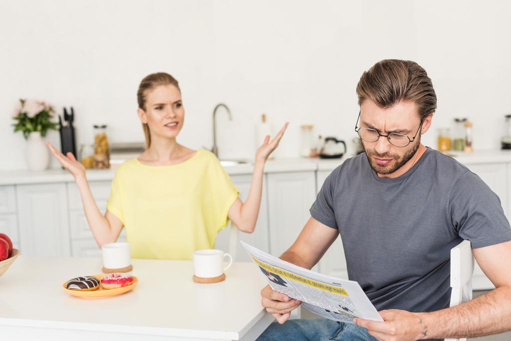 jeune femme aux bras larges regardant son petit ami tout en lisant le journal à table avec le petit déjeuner
  - Photo, image