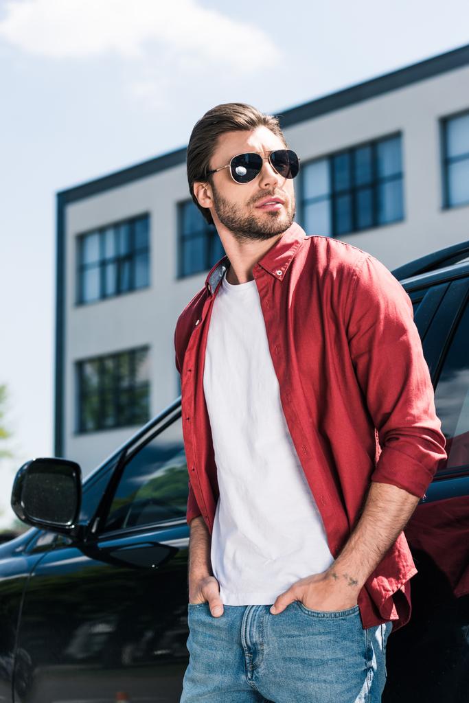 黒の車の近くに立ってのポケットに手でサングラスでスタイリッシュな男性モデル  - 写真・画像