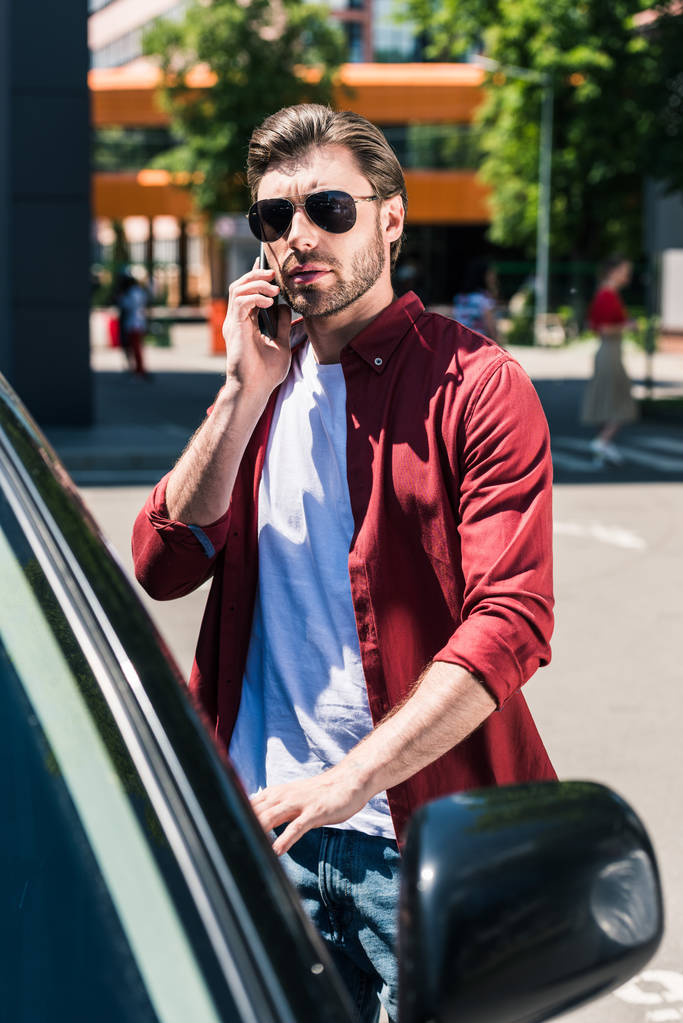 elegáns férfi napszemüveg beszél a smartphone és a saját autó ajtó városi utca  - Fotó, kép