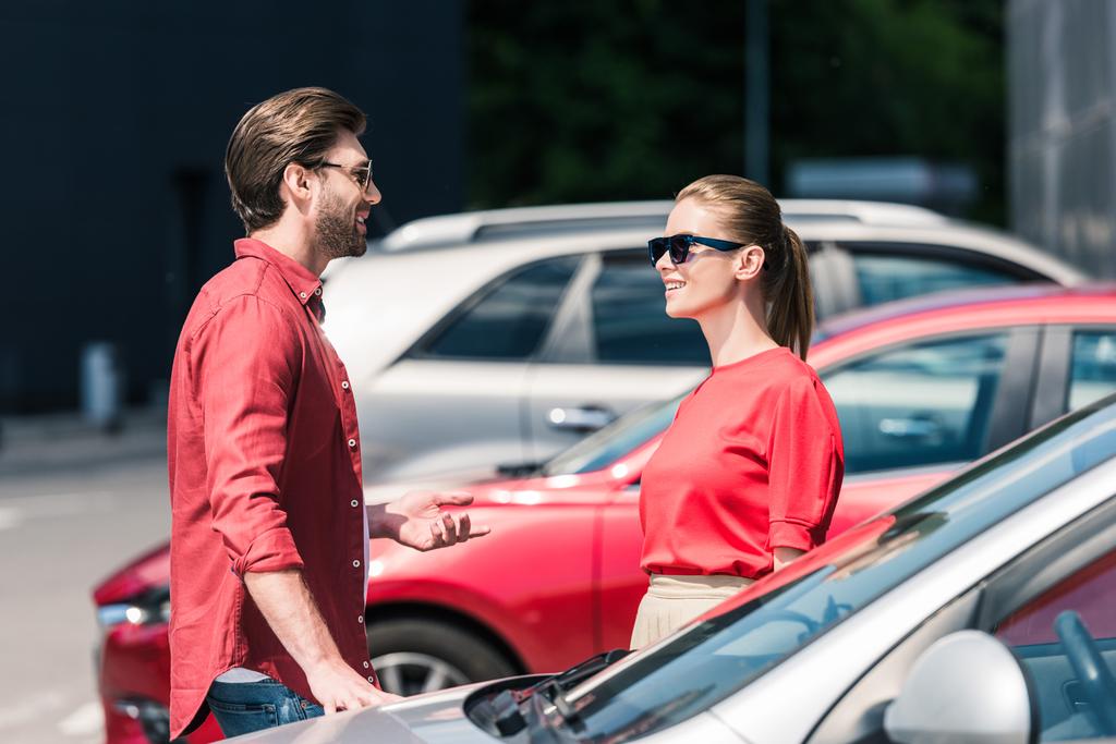 vista laterale dell'uomo elegante in occhiali da sole che parla con la ragazza vicino all'auto
  - Foto, immagini