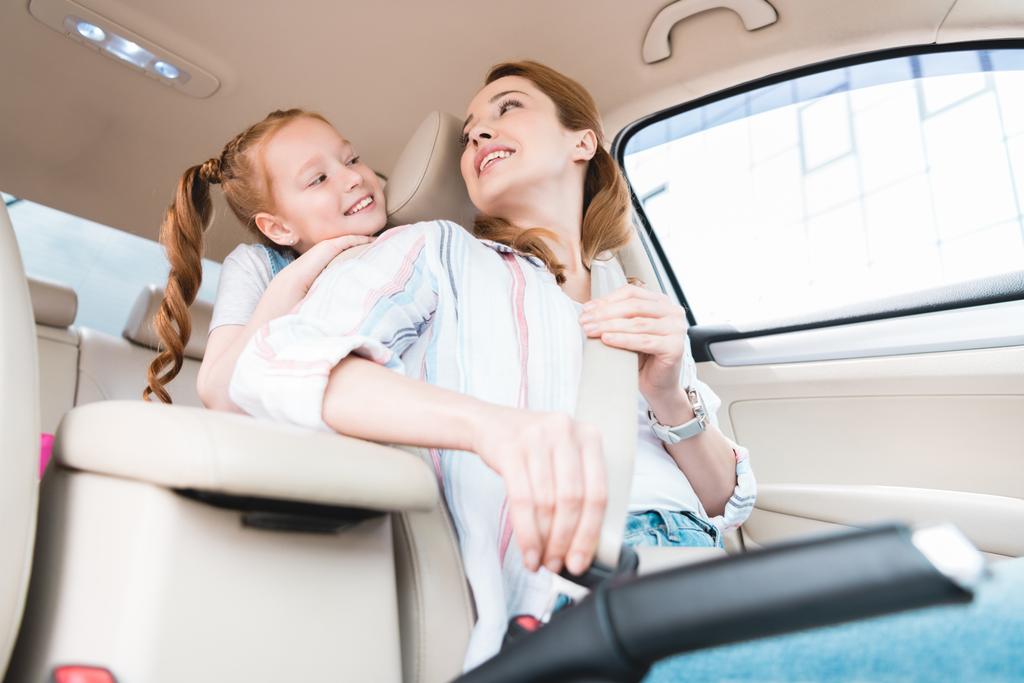 low angle view of woman fastening seat belt while driving car with daughter behind  - Photo, Image