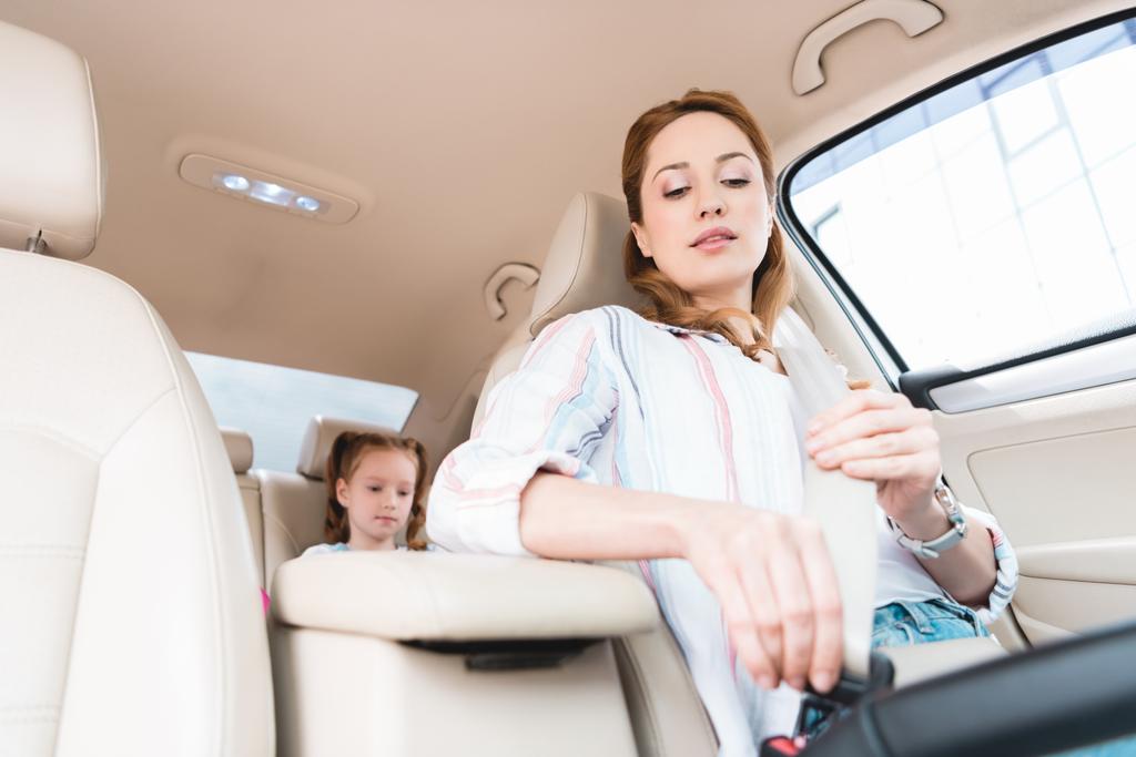 χαμηλή γωνία προβολής της γυναίκας στερέωση ζωνών ασφαλείας κατά την οδήγηση αυτοκινήτου με κόρη στο κάθισμα επιβατών - Φωτογραφία, εικόνα