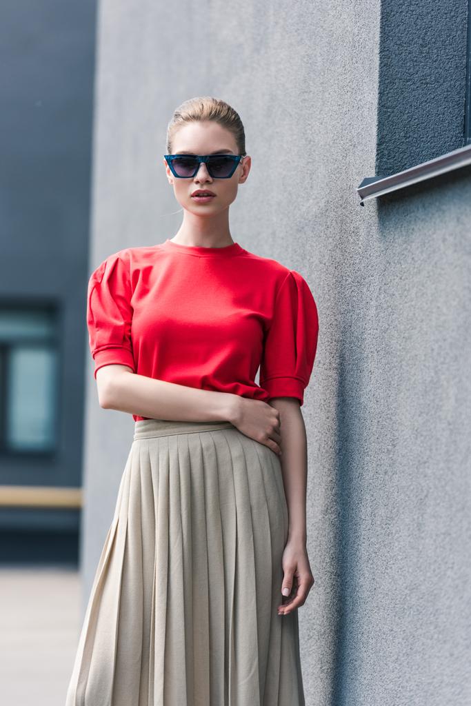 Stylisches weibliches Modell mit Sonnenbrille posiert in der Nähe von Gebäude  - Foto, Bild