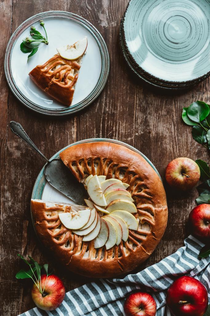 tendido plano con trozo de tarta de manzana casera, servidor de pastel y manzanas frescas en la superficie de madera
 - Foto, Imagen
