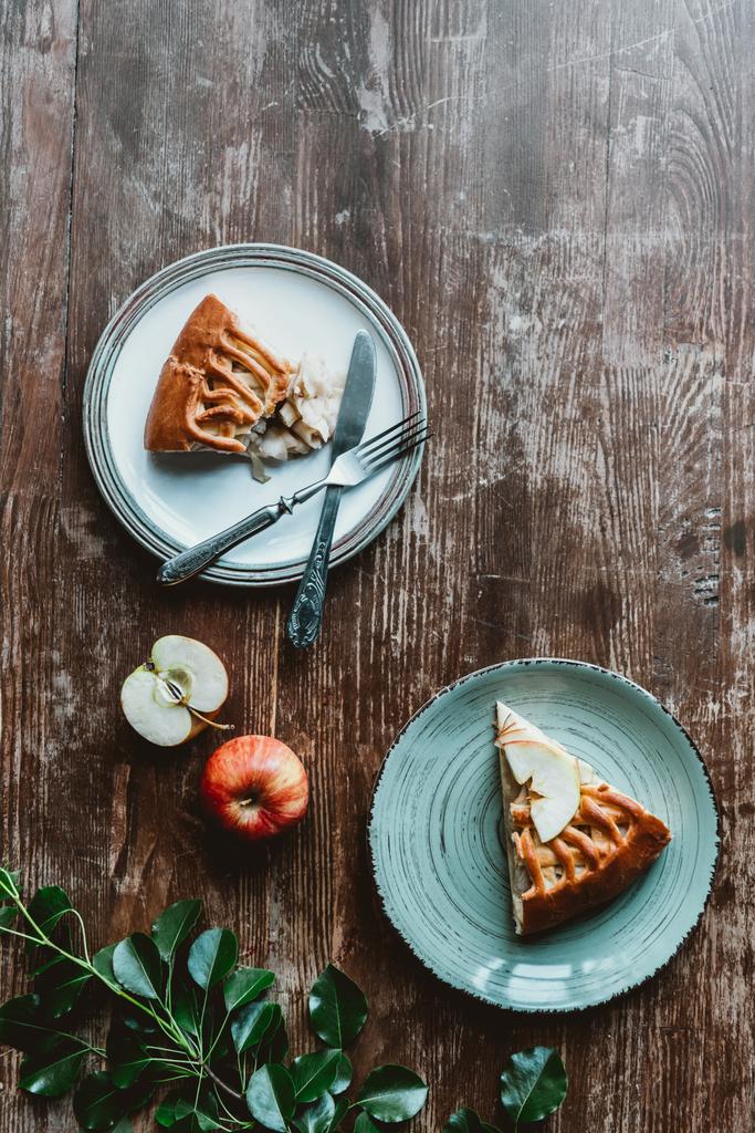 плоский лежав із шматочками яблучного пирога на тарілках, столових приборах та свіжих яблуках, розташованих на дерев'яній стільниці
 - Фото, зображення