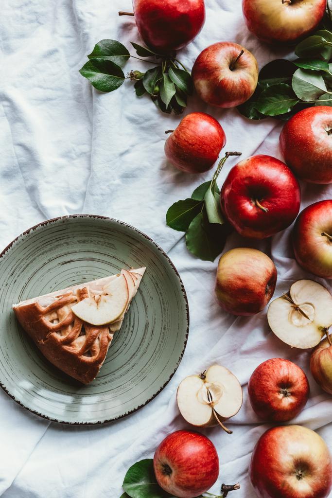 vista superior de la disposición del pedazo de pastel de manzana en el plato y manzanas frescas en mantel blanco
 - Foto, imagen