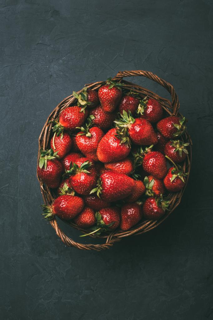 vista superior de fresas dulces frescas maduras en canasta de mimbre sobre negro
 - Foto, Imagen