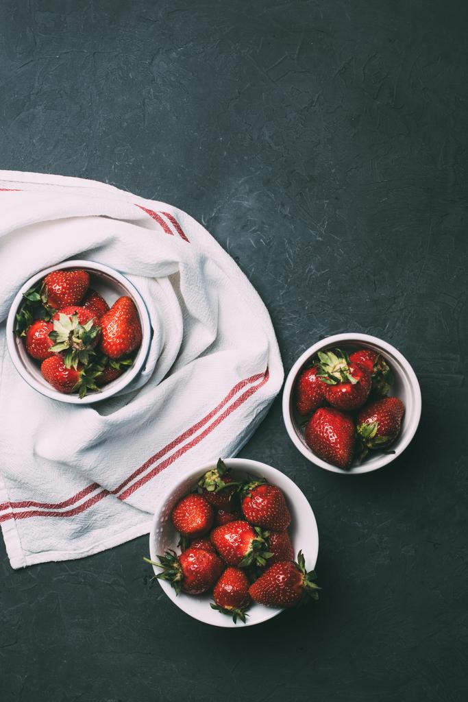 pohled shora zralé červené jahody v miskách a ručník na černém pozadí  - Fotografie, Obrázek