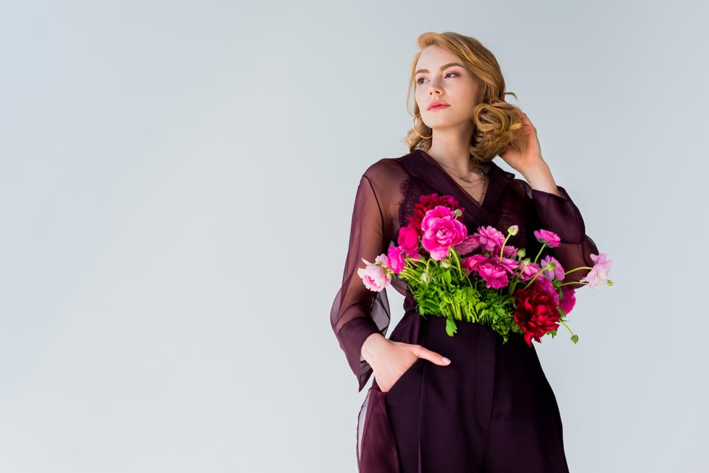 weergave van de lage hoek van elegante jongedame met mooie bloemen op zoek weg geïsoleerd op grijs - Foto, afbeelding