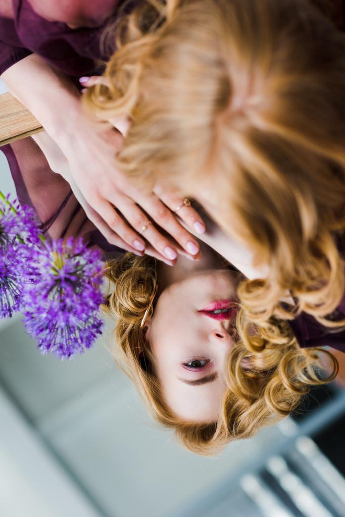 selektiver Fokus einer jungen Frau, die Spiegelung betrachtet, während sie auf einem Spiegel mit blauen Blumen liegt   - Foto, Bild