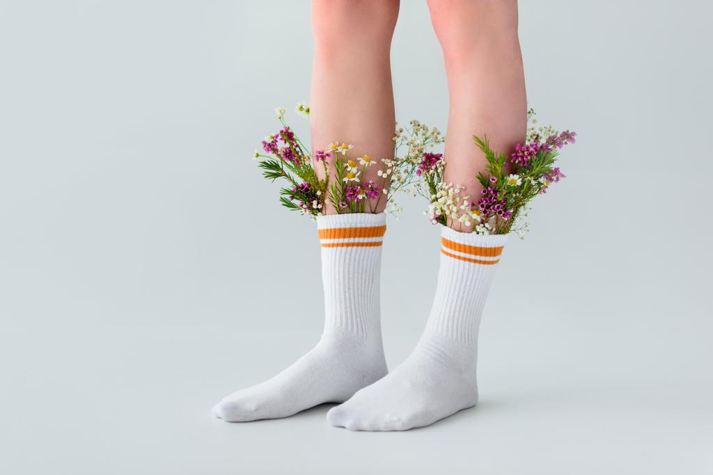 abgeschnittene Aufnahme weiblicher Beine in Socken mit frischen Blumen isoliert auf grau   - Foto, Bild