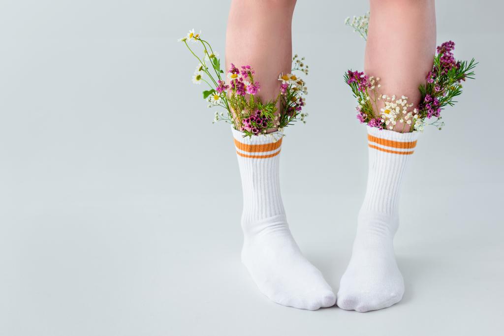 περικοπεί shot από νεαρή γυναίκα σε κάλτσες με όμορφα λουλούδια που στέκεται απομονωθεί σε γκρι   - Φωτογραφία, εικόνα