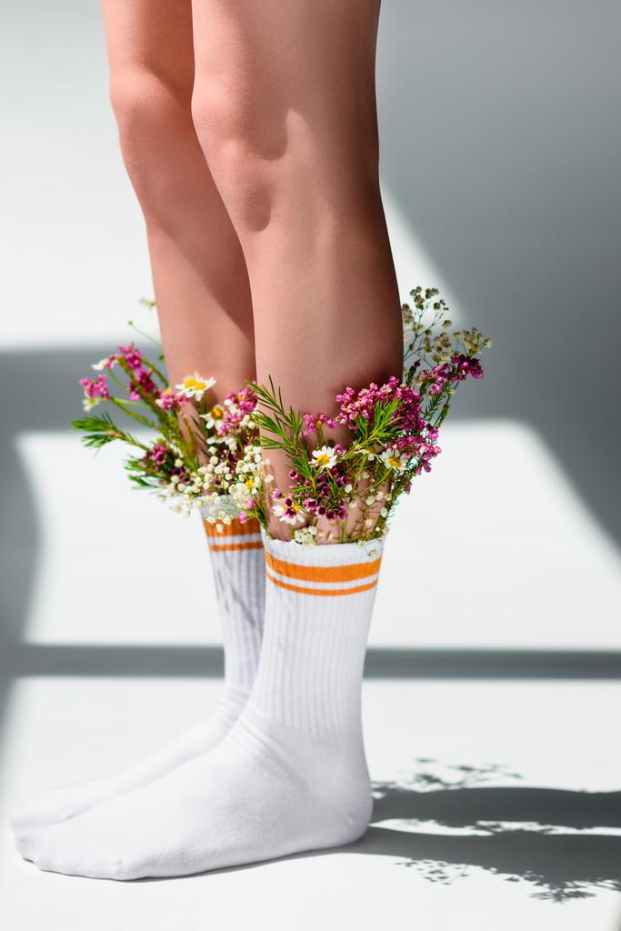 close-up partial view of young woman with beautiful flowers in socks standing on grey - Photo, Image