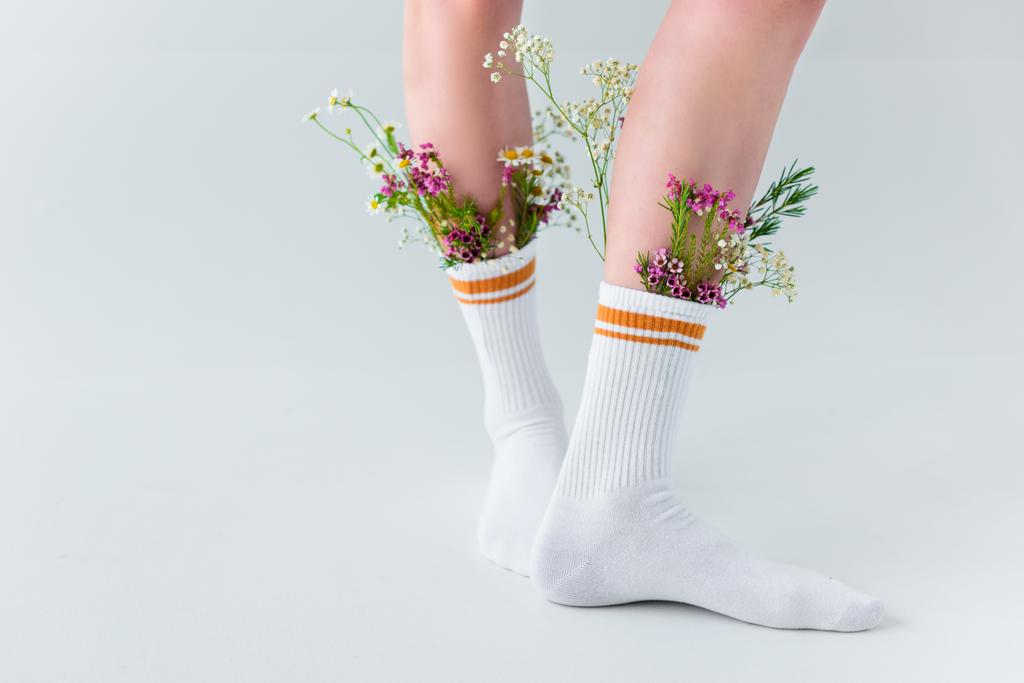 szczegół częściowy widok kobiece nogi ze świeżymi kwiatami w skarpety na białym tle na szary - Zdjęcie, obraz