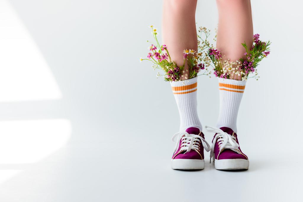 bijgesneden schot van meisje met verse bloemen in sokken op grijs - Foto, afbeelding
