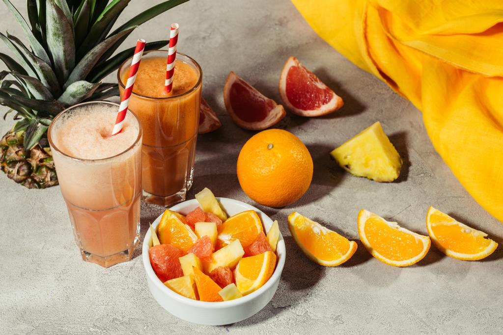 Glasses with tropical fruits juice and citrus pieces on grey table - Photo, Image