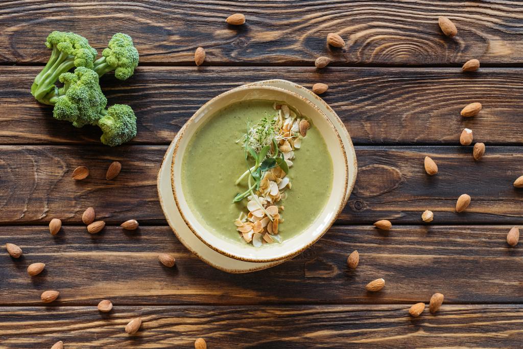 düz lay ile görücü usulü taze brokoli, badem ve ahşap masa üzerinde vejetaryen krem çorba - Fotoğraf, Görsel