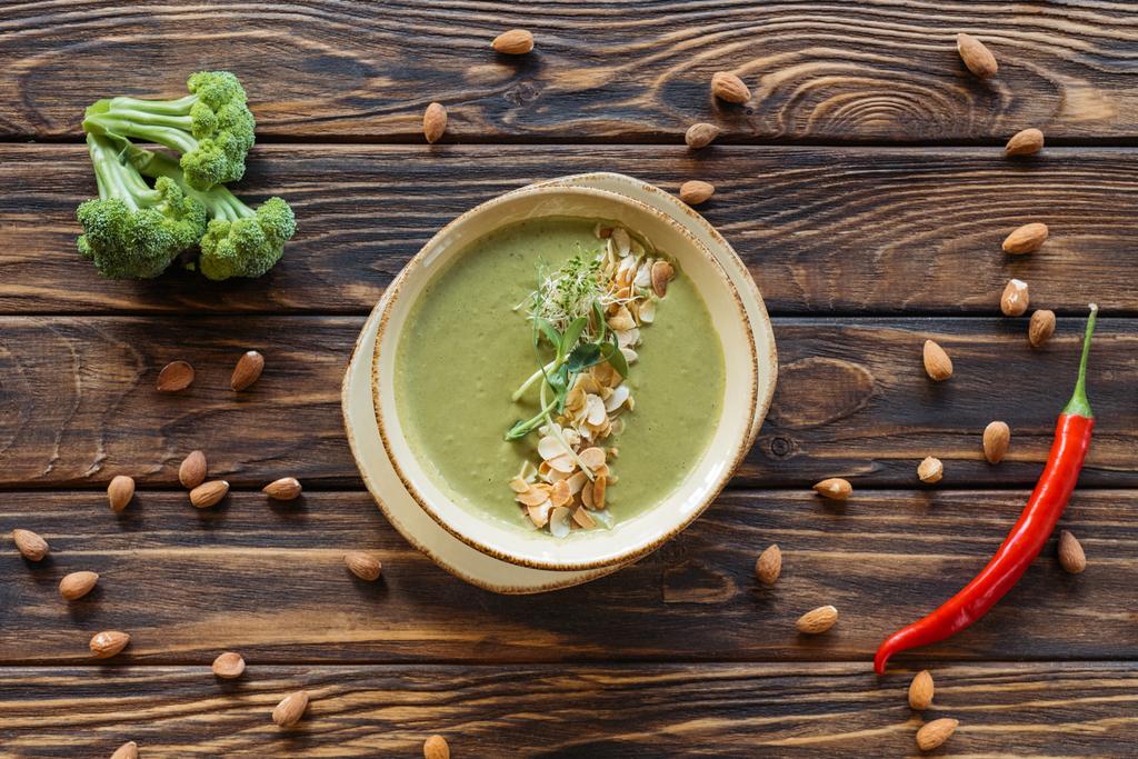 top view of arranged vegetarian cream soup, fresh broccoli, almonds and chili peppers on wooden surface - Photo, Image