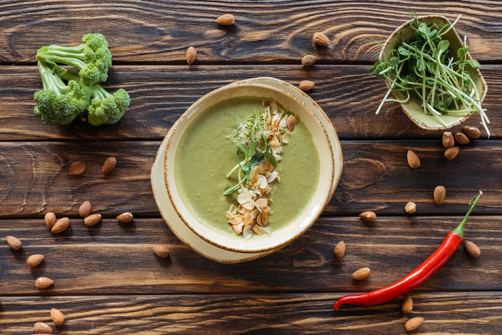ahşap yüzeyde görücü usulü vejetaryen krem çorbası, taze brokoli, badem ve biber üstten görünüm - Fotoğraf, Görsel