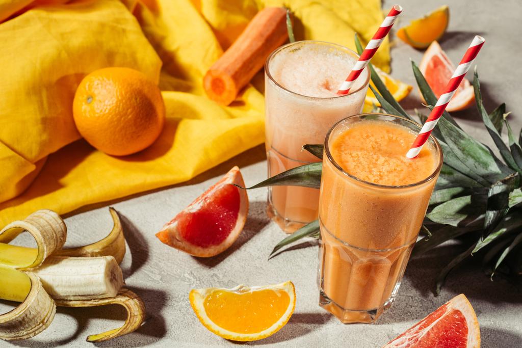 Bicchieri con succo di frutta tropicale e pezzi di frutta sulla tavola grigia
 - Foto, immagini