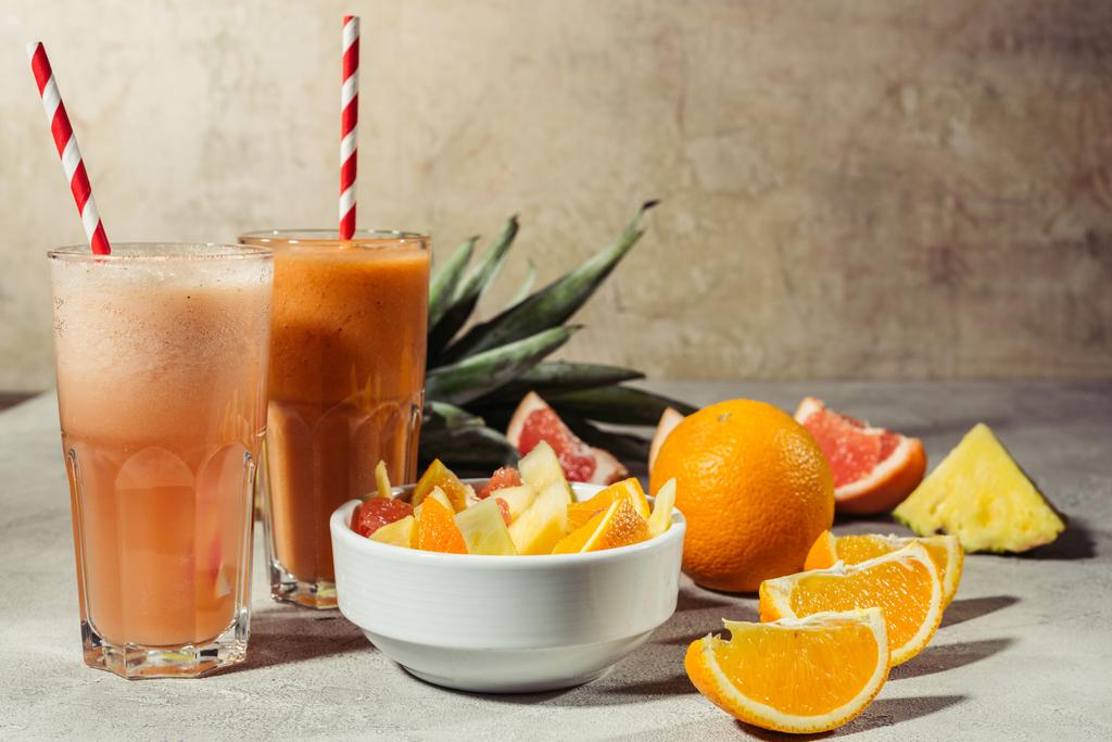 Очки с цитрусовыми соками и фруктами на сером столе
 - Фото, изображение