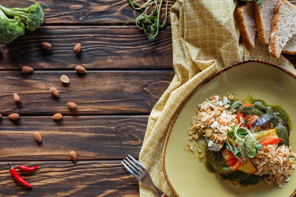 vlakke leggen met vegetarische salade met geraspte amandelen, stukjes brood, chilipepers en linnen op houten tafelblad - Foto, afbeelding