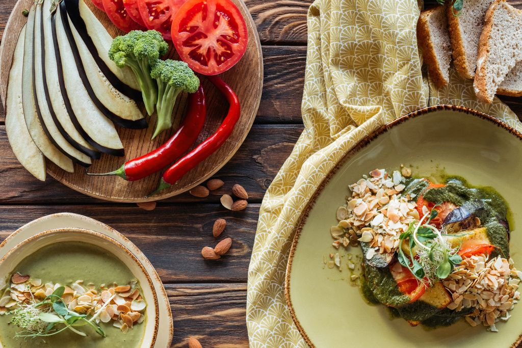 フラットは、ベジタリアン サラダ、クリーム スープを置き、木製のテーブルの上の周りの新鮮な食材をアレンジ - 写真・画像