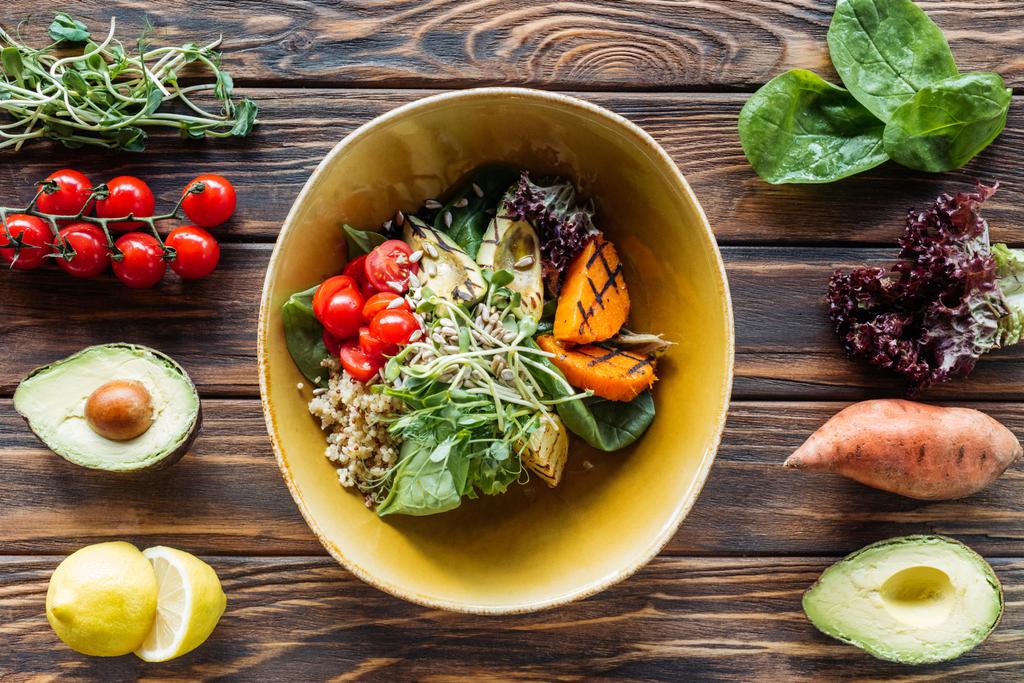 flat lay com salada vegetariana com legumes grelhados, brotos, tomates cereja na tigela e ingredientes frescos dispostos em torno de mesa de madeira
 - Foto, Imagem