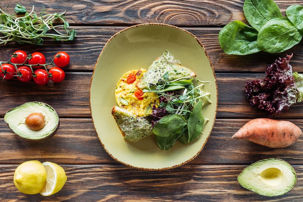 flat lay with vegetarian salad served on plate and fresh ingredients arranged around on wooden tabletop - Photo, Image