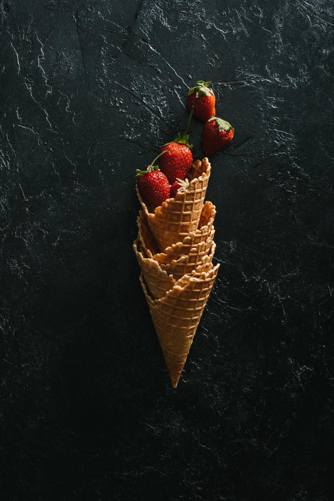 Morangos maduros em cones de waffle empilhados em fundo escuro
 - Foto, Imagem