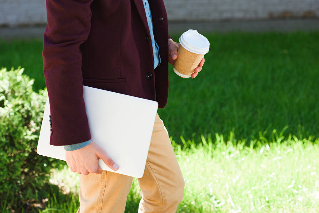 Oříznout záběr člověka s notebookem a papíru pohár chůzi venku - Fotografie, Obrázek
