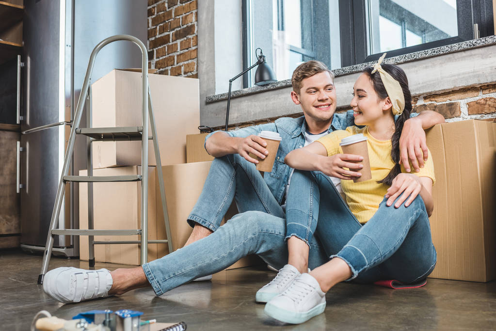 interracial fiatal pár papír csésze kávé ülő földre új otthonába mozgás közben - Fotó, kép