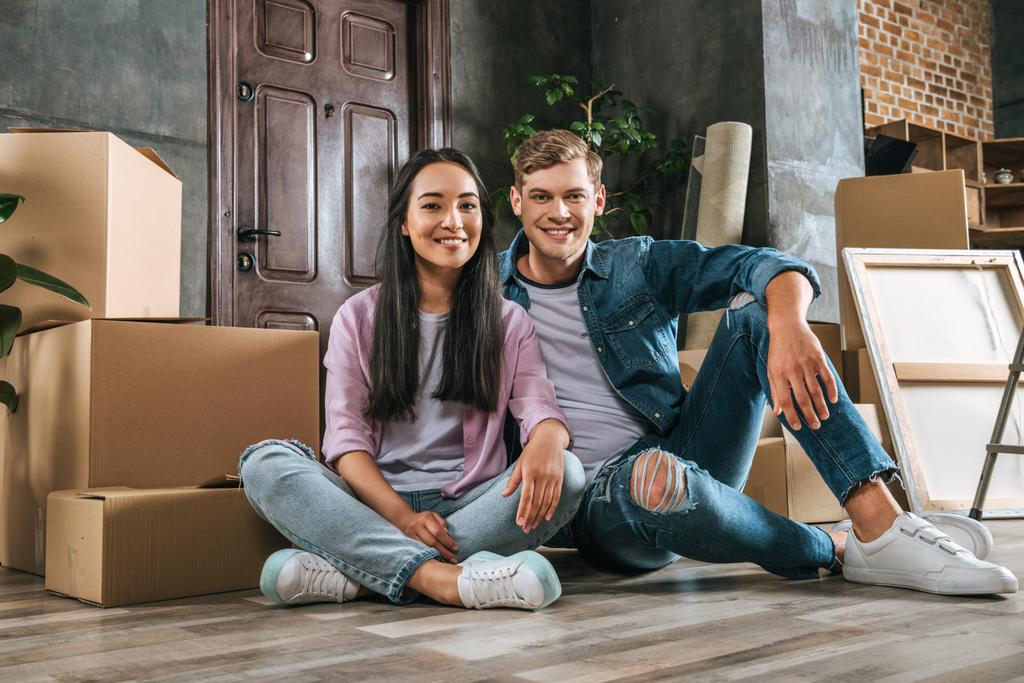 attraktives junges Paar sitzt beim Einzug in neues Zuhause zusammen auf dem Boden - Foto, Bild