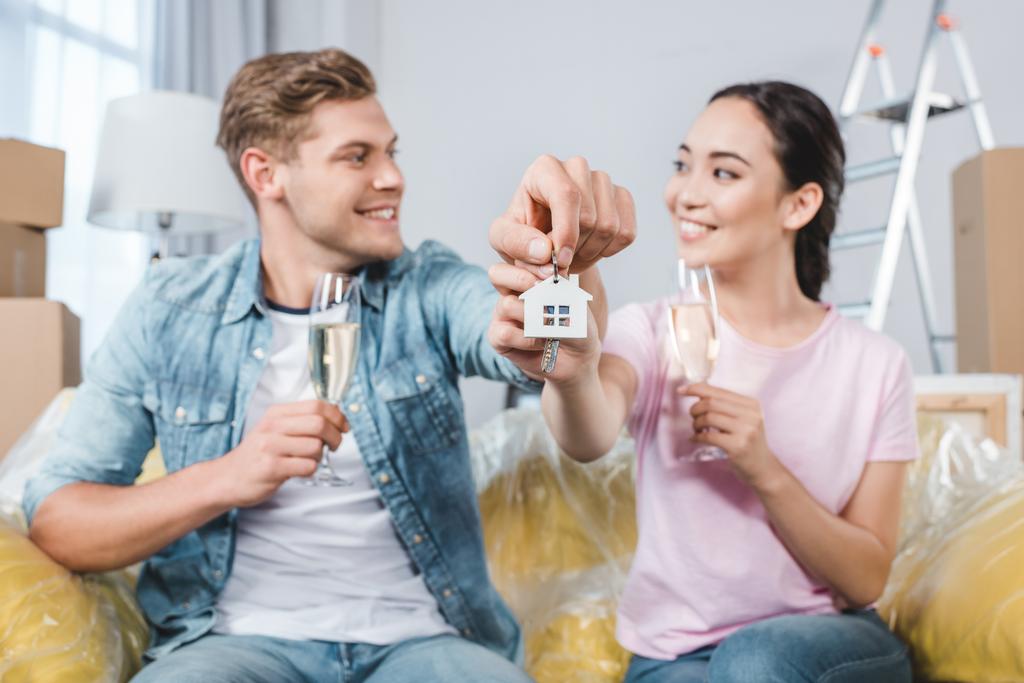 bella giovane coppia con bicchieri di champagne e chiavi seduti sul divano dopo il trasferimento in una nuova casa
 - Foto, immagini